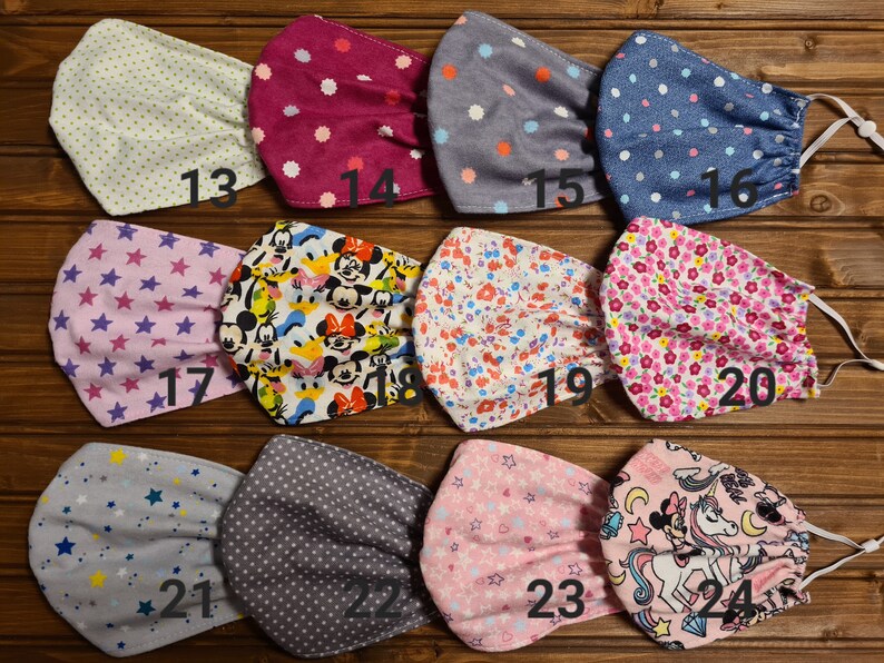 May include: Twenty-four different fabric face masks with various patterns, including polka dots, stars, flowers, and cartoon characters. The masks are numbered 13 through 24.