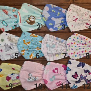 May include: Twelve different fabric face masks with various colorful patterns and designs. The masks are made of cotton and have elastic ear loops. The patterns include butterflies, sloths, foxes, bunnies, hearts, and unicorns. The masks are numbered 1 through 12.