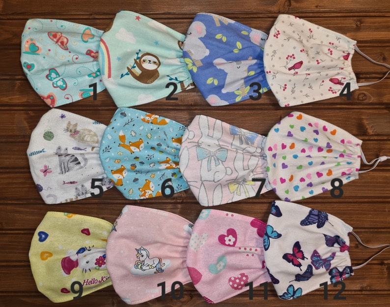 May include: Twelve different fabric face masks with various colorful patterns and designs. The masks are made of cotton and have elastic ear loops. The patterns include butterflies, sloths, foxes, bunnies, hearts, and unicorns. The masks are numbered 1 through 12.
