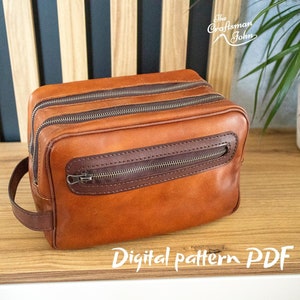 Puede incluir: Un neceser de cuero marrón con dos compartimentos con cremallera y un asa superior. El neceser está sobre una superficie de madera. "Digital pattern PDF" está escrito en blanco sobre la superficie.