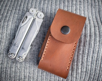 May include: A silver multi-tool with the text "Leatherman" on the handle, in a brown leather case with a snap closure.