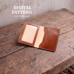 May include: A brown leather wallet featuring a clear ID window slot on the left and three curved card slots on the right, with visible stitching along the edges. The text DIGITAL PATTERN PDF DOWNLOAD is printed in white above the wallet.
