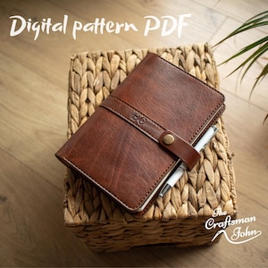 May include: A brown leather journal with a strap closure and a pen, resting on a woven basket. The text "Digital pattern PDF" is at the top, and "The Craftsman John" is at the bottom right.