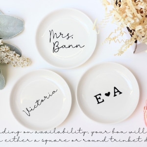 Puede incluir: Tres platos redondos de cer&aacute;mica blanca con letras negras. Los platos son redondos y tienen el siguiente texto: "Mrs. Bann", "Victoria" y "E&hearts;A".