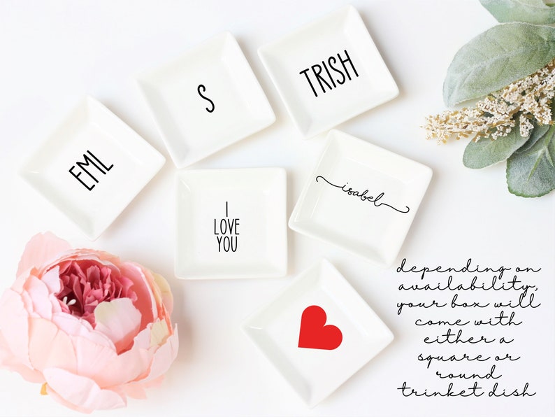 May include: Six white square trinket dishes with various designs. The designs include the words "EML", "S", "TRISH", "I LOVE YOU", "isabel", and a red heart. The dishes are arranged on a white surface.
