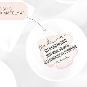 May include: A white ceramic dish with a pink watercolour design that says "madrina UN REGALO ENVIADO DESDE ARRIBA, UN &Aacute;NGEL DE LA GUARDA QUE FUE ELEGIDO CON amor".