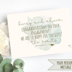 Puede incluir: Una tarjeta de estilo acuarela con un fondo de acuarela verde y azul. La tarjeta dice "henry and alicia, CONGRATULATIONS ON YOUR ENGAGEMENT! WE ARE SO HAPPY FOR YOU GUYS! - the merits".