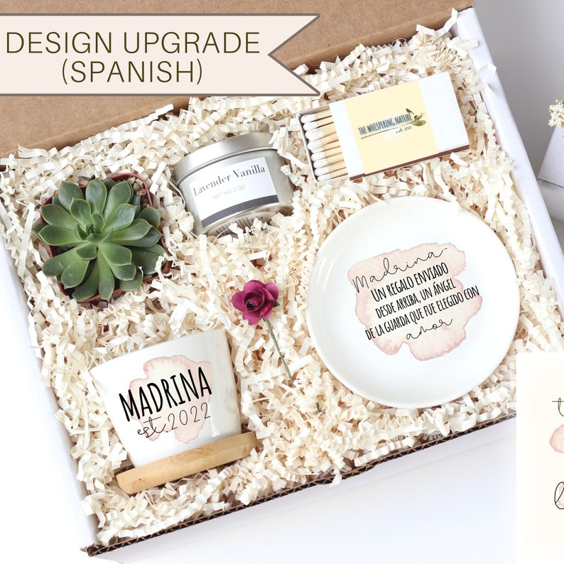 May include: A gift box filled with items for a godmother, including a succulent plant, a small candle, matches, a small dish with a message in Spanish, and a small pot with the word "Madrina" and the year "2022" on it.