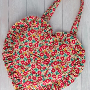 May include: A red, yellow, and blue floral print tote bag with a ruffled edge and a heart-shaped design. The bag has a single strap.