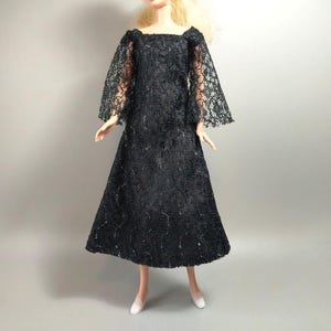 May include: A black lace dress with a square neckline and bell sleeves. The dress has a sparkly texture and is perfect for a formal occasion.