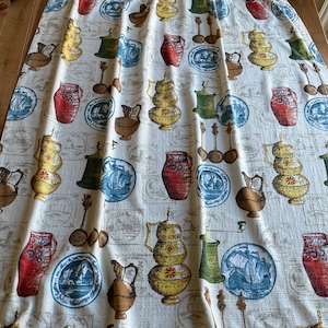 May include: A white fabric curtain with a repeating pattern of blue and white plates, red and yellow pitchers, and brown jugs. The fabric has a subtle texture and a cream background.