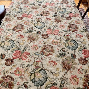 May include: A beige tablecloth with a floral pattern featuring red, green, and brown flowers. The tablecloth has a subtle texture and a repeating pattern.