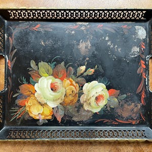 Peut inclure: Plateau rectangulaire en métal noir avec un motif floral. Le plateau présente un bouquet peint de roses blanches et jaunes avec des feuilles vertes et rouges. Les bords ont un motif ajouré décoratif et des poignées.