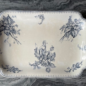Op de afbeelding: Een rechthoekige witte serveerschaal met een blauw bloemenmotief. De schaal heeft een gegolfde rand en een decoratieve rand.
