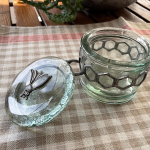 Groen glazen getinte honingpot met deksel versierd met een zilverkleurig metalen honingraatraster en een bij op het deksel