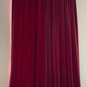 Könnte beinhalten: Burgunderfarbene Samtvorhänge, die an einer weißen Stange hängen. Die Vorhänge sind geschlossen, mit vertikalen Falten, die ein strukturiertes Aussehen erzeugen. Die satte Farbe und das weiche Material deuten auf einen luxuriösen Einrichtungsgegenstand hin.