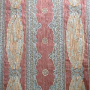 May include: Close-up of a patterned fabric with a peach background. Vertical stripes feature ornate designs in gold, silver, and peach. The fabric has a textured appearance, with repeating floral and geometric patterns.