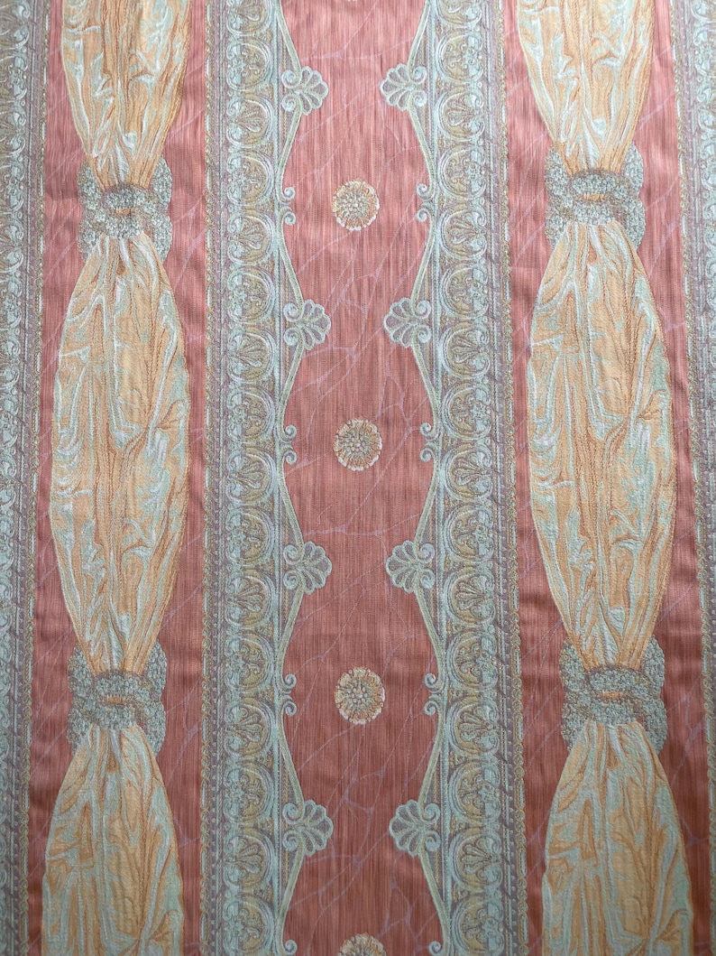 May include: Close-up of a patterned fabric with a peach background. Vertical stripes feature ornate designs in gold, silver, and peach. The fabric has a textured appearance, with repeating floral and geometric patterns.