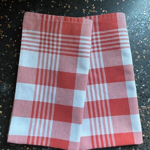 May include: Two red and white gingham kitchen towels. The towels are folded in half and are lying on a black surface.