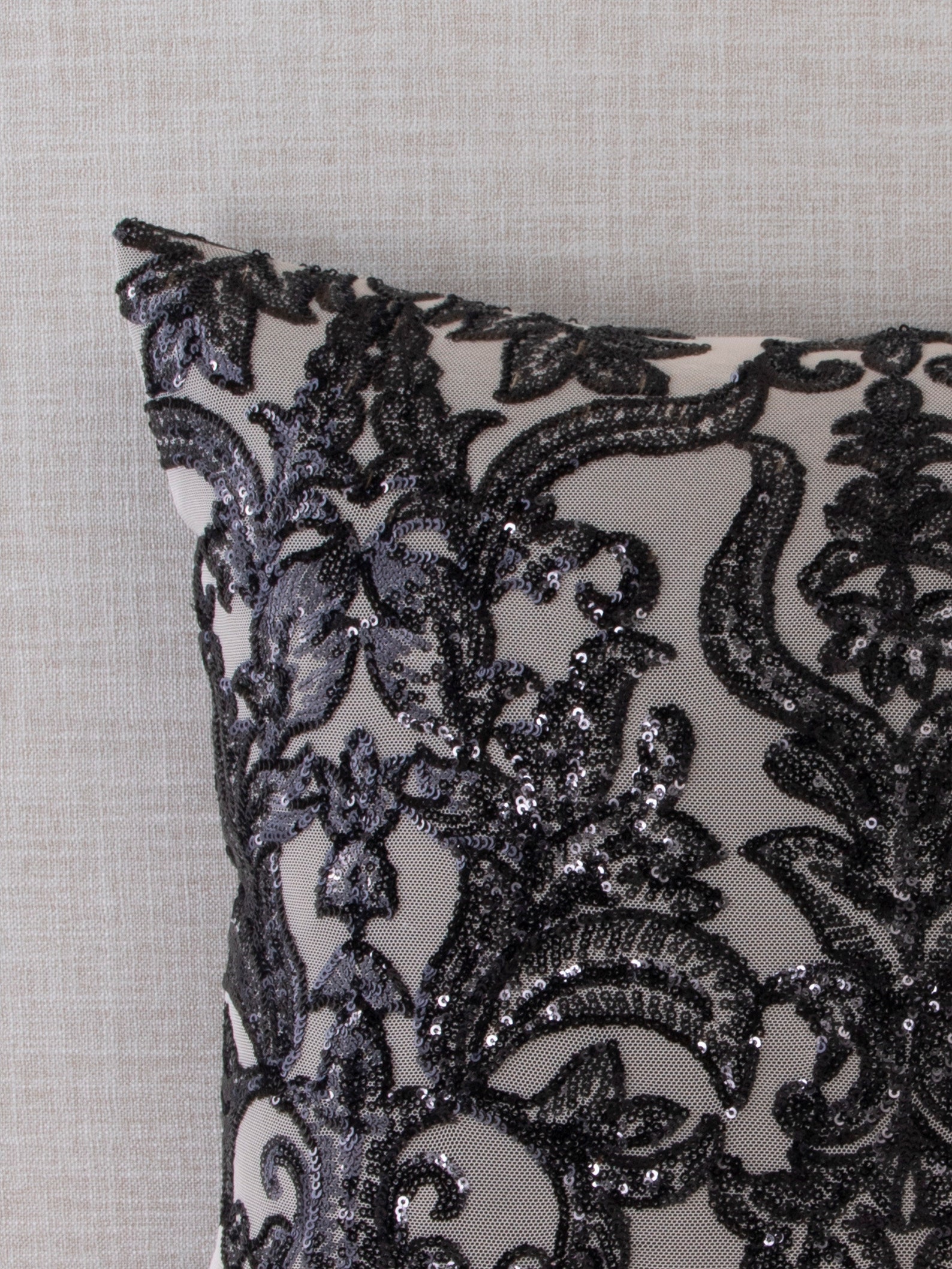 Close-up of a gray throw pillow with intricate black damask sequin embroidery, showcasing the detailed texture and shimmer of the design against a light fabric background