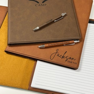 Peut inclure: Un classeur en similicuir marron avec un bloc-notes et deux stylos. Le classeur porte un logo avec un "S" stylis&eacute; et le mot "CAMP" en dessous. Le bloc-notes porte le nom "Jackson Smith" et le titre "Directeur des ressources humaines" &eacute;crit dessus.