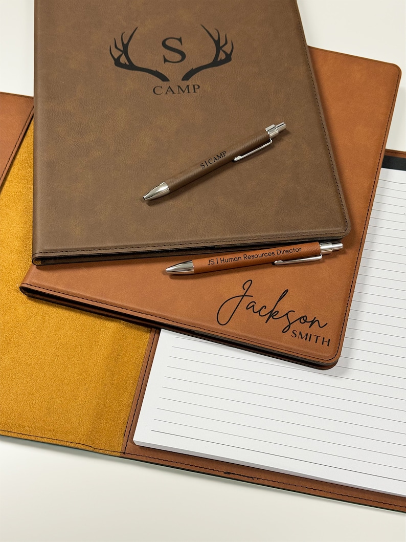 Peut inclure: Un classeur en similicuir marron avec un bloc-notes et deux stylos. Le classeur porte un logo avec un "S" stylis&eacute; et le mot "CAMP" en dessous. Le bloc-notes porte le nom "Jackson Smith" et le titre "Directeur des ressources humaines" &eacute;crit dessus.