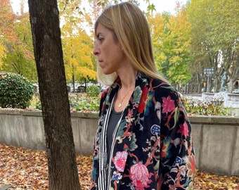 May include: A black velvet jacket with a floral print in shades of pink, red, green, and blue. The jacket has a long, flowing silhouette and a shawl collar.
