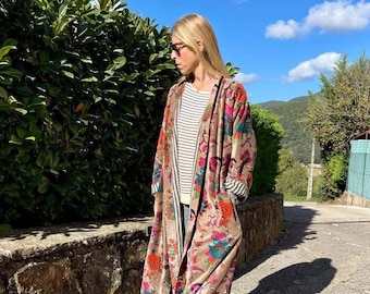 Puede incluir: Una bata larga con estampado floral y forro a rayas. La bata es de color marrón claro con flores rosas, naranjas y azules. La modelo lleva la bata con una camisa a rayas debajo y unos vaqueros azules.