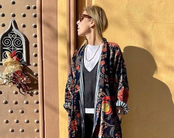 Peut inclure: Une femme portant une longue robe noire à imprimé floral avec un t-shirt blanc en dessous. Elle porte un pantalon noir et des baskets noires et blanches.