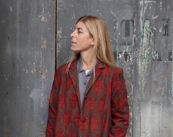 May include: A brown blazer with a red floral pattern. The blazer has a single button closure and a collar. The person is wearing black pants.