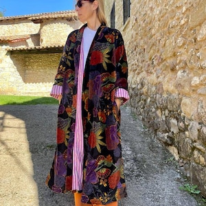 May include: A long black velvet robe with a floral print in shades of red, orange, yellow, purple, and green. The robe has a pink and white striped lining and a black collar.