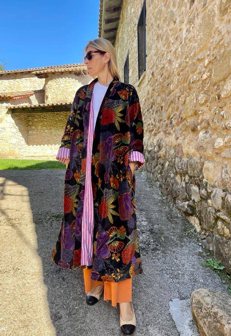 May include: A long black velvet robe with a floral print in shades of red, orange, yellow, purple, and green. The robe has a pink and white striped lining and a black collar.