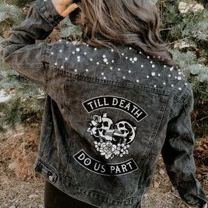 May include: A black denim jacket with pearl embellishments on the shoulders. The back of the jacket features a white patch with the text "Till Death Do Us Part" and a graphic of two skulls in a heart with flowers.