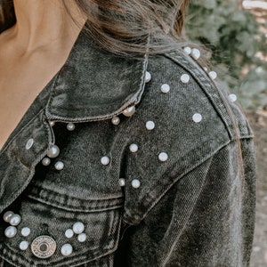 K&ouml;nnte beinhalten: Eine schwarze Jeansjacke mit Perlenbesatz an Schultern und Taschen.