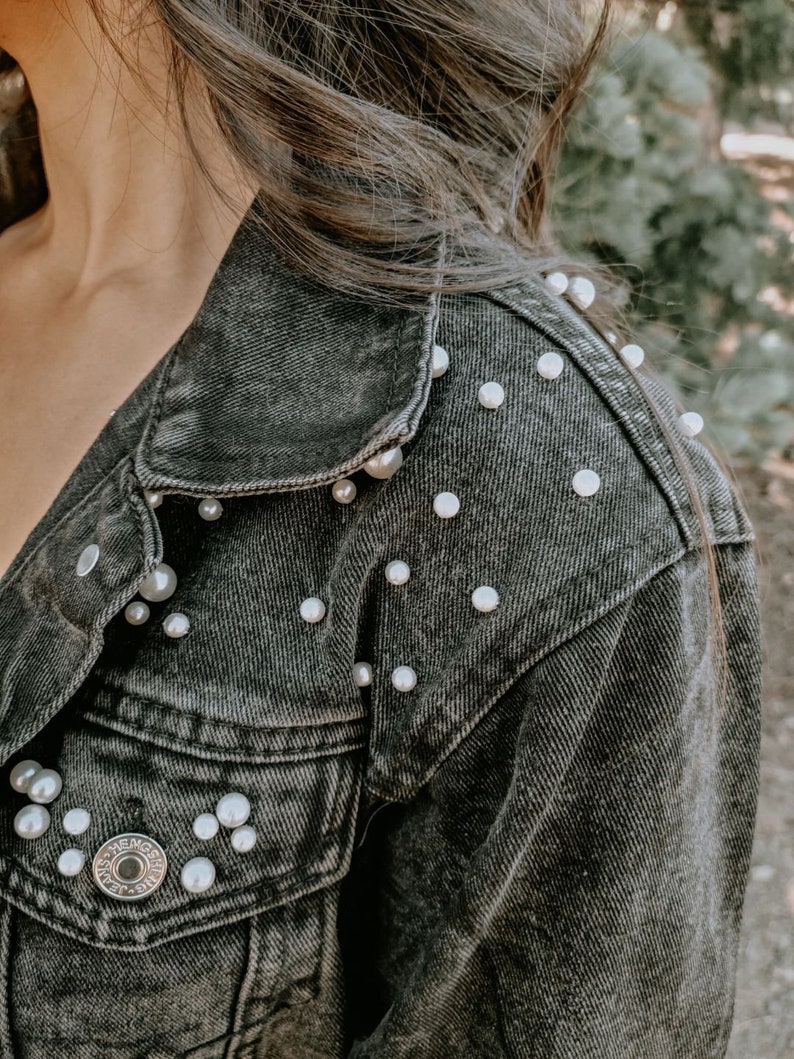 K&ouml;nnte beinhalten: Eine schwarze Jeansjacke mit Perlenbesatz an Schultern und Taschen.