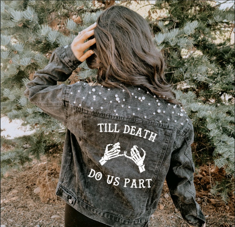 K&ouml;nnte beinhalten: Eine schwarze Jeansjacke mit Perlenbesatz und einem wei&szlig;en Aufdruck auf der R&uuml;ckseite, der "Till Death Do Us Part" mit zwei Skeletth&auml;nden, die einen kleinen Fingerversprechen machen, lautet.