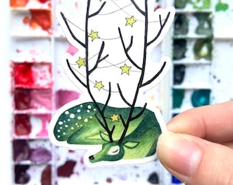 May include: A green deer with white spots is sleeping under a tree with a string of lights. The lights are yellow stars. The deer has antlers with a star on top.