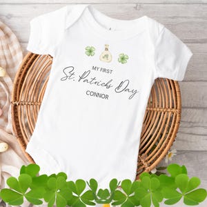 May include: White baby onesie with the text "My First St. Patricks Day Connor" and a green shamrock design.