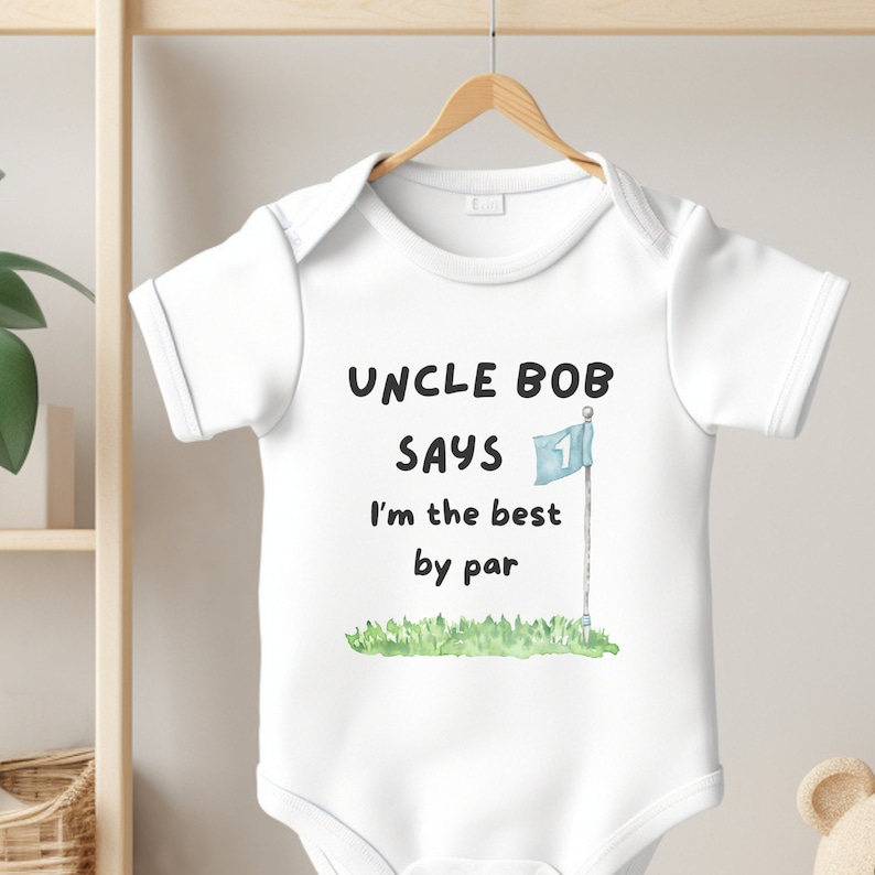 May include: White baby onesie with the text "UNCLE BOB SAYS I'm the best by par." A watercolor illustration of a golf flag on a green field is below the text. The onesie is hanging on a wooden hanger.