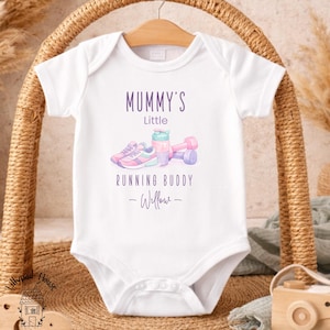Può includere: Body da bambino bianco con la scritta "Mummy's Little Running Buddy" in viola, insieme a un'illustrazione ad acquerello di scarpe da ginnastica, una borraccia e manubri. Il nome "Willow" è sotto.