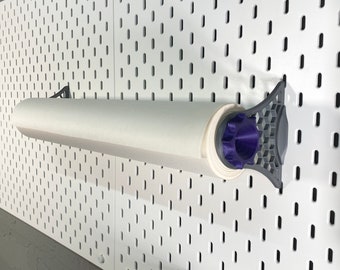 Könnte beinhalten: Ein weißer Papierrollenhalter, montiert an einer weißen Lochwand. Der Halter hat graue Halterungen und ein lila Endstück. Die Papierrolle ist weiß. Die Lochwand hat gleichmäßig verteilte Löcher.