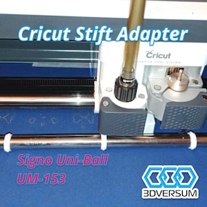 Könnte beinhalten: Nahaufnahme einer Cricut-Schneidemaschine mit einem Signo Uni-Ball UM-153 Stift, der in den Werkzeughalter eingesetzt ist. Der Stift wird durch einen weißen Adapter gehalten. Die Maschine steht auf einer blauen Oberfläche.