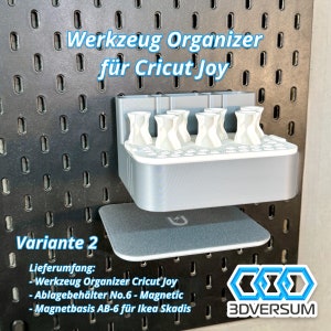 May include: A gray 3D-printed tool organizer for Cricut Joy, mounted on a black pegboard. The organizer has multiple white holders and a magnetic base. Text on the image reads "Werkzeug Organizer f&uuml;r Cricut Joy" and "Variante 2".