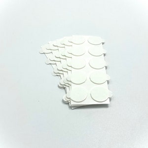 Peut inclure: Une pile de points adh&eacute;sifs blancs, chacun ayant une forme ronde et un bord l&eacute;g&egrave;rement sur&eacute;lev&eacute;. Les points sont dispos&eacute;s en rang&eacute;es et en colonnes sur un fond blanc.