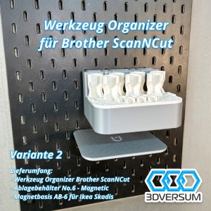 May include: A gray and white tool organizer for Brother ScanNCut, mounted on a black pegboard. The organizer has multiple compartments and is labeled "Variante 2". Includes the text "3DVERSUM".