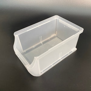 Può includere: Un contenitore di stoccaggio in plastica trasparente con un bordo anteriore leggermente inclinato. Il contenitore è vuoto e ha una finitura liscia e lucida.