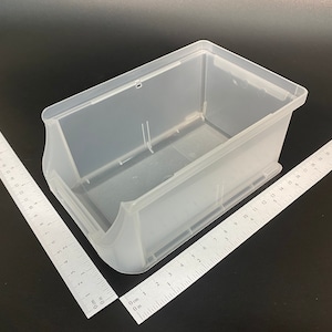 May include: A clear plastic storage container, rectangular with curved sides and a handle cutout. Two rulers are angled towards the bin. The container is empty, against a dark background. Measurements are in centimetres.