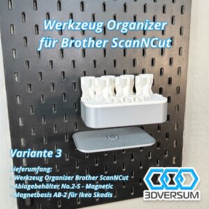 May include: A black pegboard with a white and gray organizer for Brother ScanNCut tools. The organizer holds several white tool holders. A gray magnetic base is below the organizer. Text on the board reads "Werkzeug Organizer f&uuml;r Brother ScanNCut" and "Variante 3".