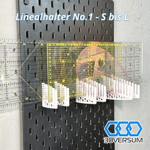 Op de afbeelding: Een zwart pegboard met transparante linialen en witte houders. De linialen hebben gele en rode markeringen. De tekst "Linealhalter No.1 - S bis L" staat bovenaan. Het logo "3DVERSUM" staat onderaan.