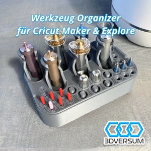 Könnte beinhalten: Grauer 3D-gedruckter Organizer für Cricut Maker und Explore Werkzeuge. Er hat Steckplätze für verschiedene Werkzeuggrößen und ein Fach für kleinere Werkzeuge. Der Organizer ist mit "Werkzeug Organizer für Cricut Maker & Explore" beschriftet und trägt das 3DVersum Logo.